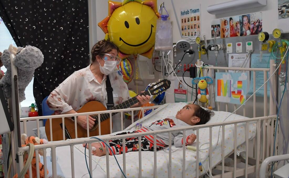 A music therapist at a child's bedside at The Children's Hospital at Westmead